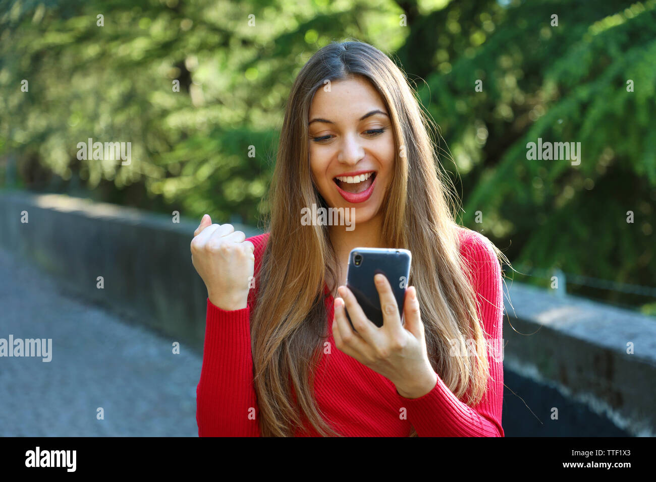 Euphorisch Frau gerade Ihre Smart Phone und zeigt Sieger Geste outdoor Stockfoto