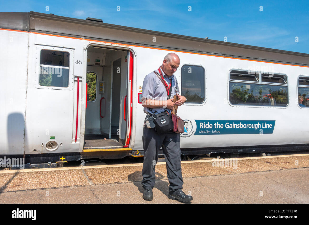 Männer mittleren Alters Mitarbeiter tragen Fahrkartenautomaten, auf der Plattform mit Passagieren an Bord und Zug zum Bahnhof West Runton, Norfolk, England verlassen. Stockfoto