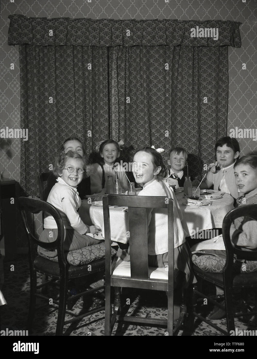 1950er Jahre, historische, genießen eine Geburtstagsfeier... Glücklich, aufgeregt, kleinen Kindern Spaß zusammen an einem Tuch bedeckt Tabelle in einem Haus, England, Großbritannien sitzen. Stockfoto