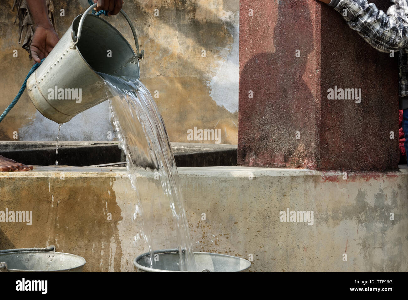 Ein indischer Junge ist das Gießen von Wasser aus einem Eimer. Stockfoto