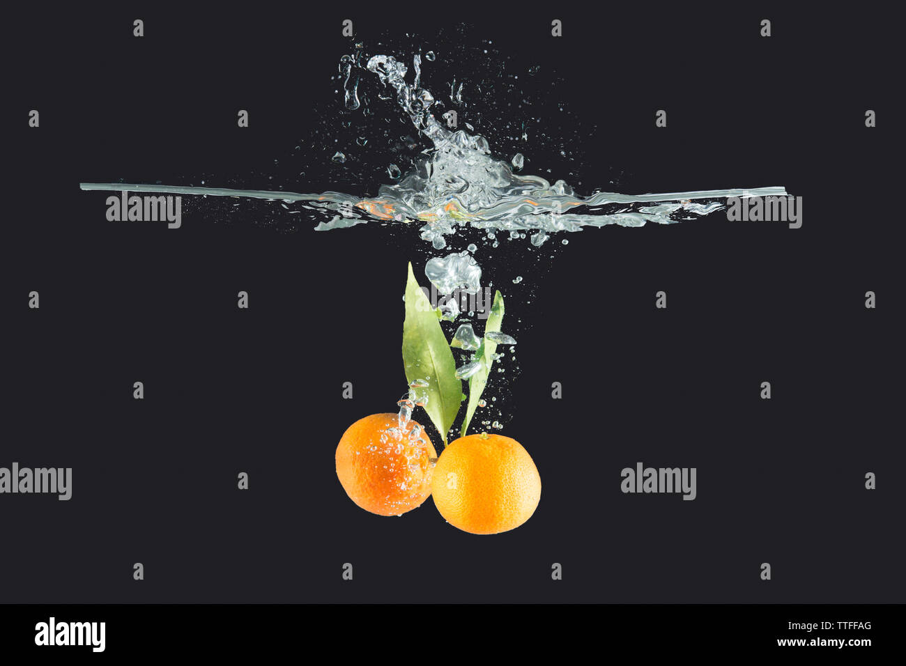 Mandarinen mit Blätter in Wasser auf dunklem Hintergrund geworfen Stockfoto