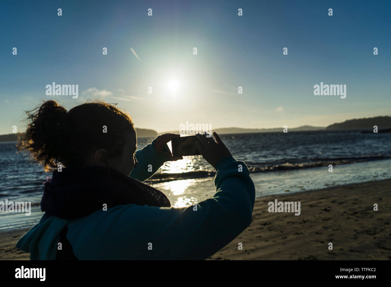 Silhouette Frau fotografieren durch Smartphone im stehen am Strand gegen Himmel Stockfoto