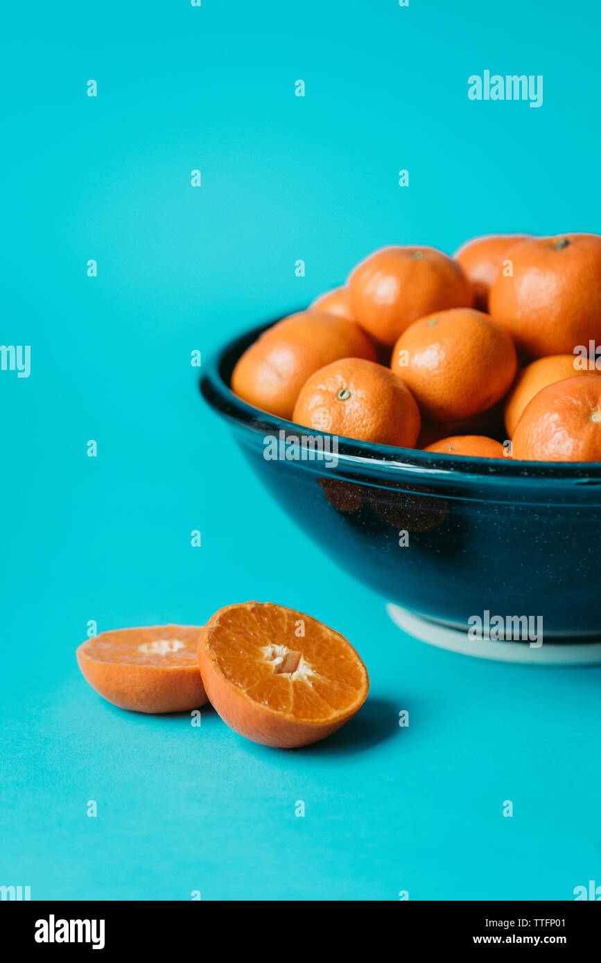 Mandarin Orange in der Hälfte durch eine Schale von Orangen auf blauem Hintergrund. Stockfoto