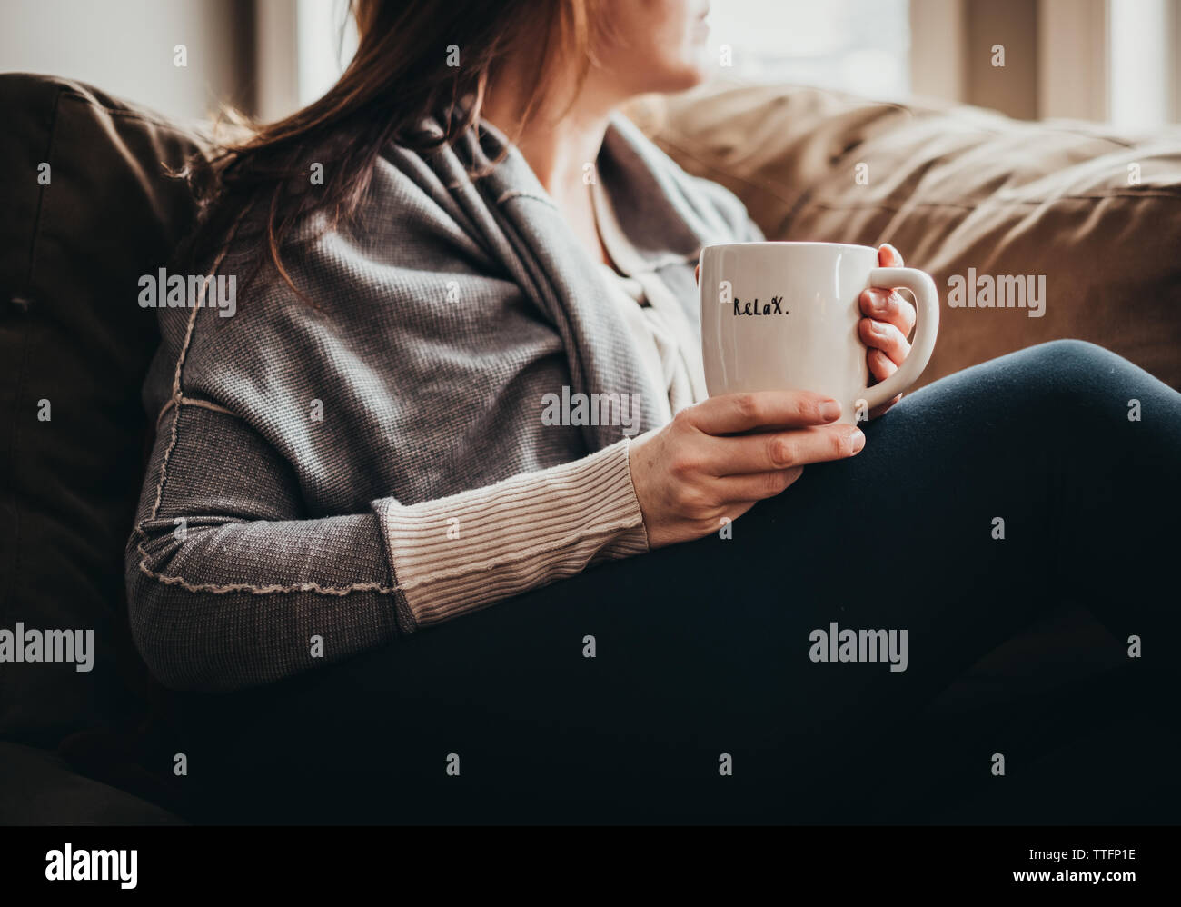 Zugeschnittenes Bild der Frau mit Becher mit Wort auf es auf der Couch entspannen. Stockfoto