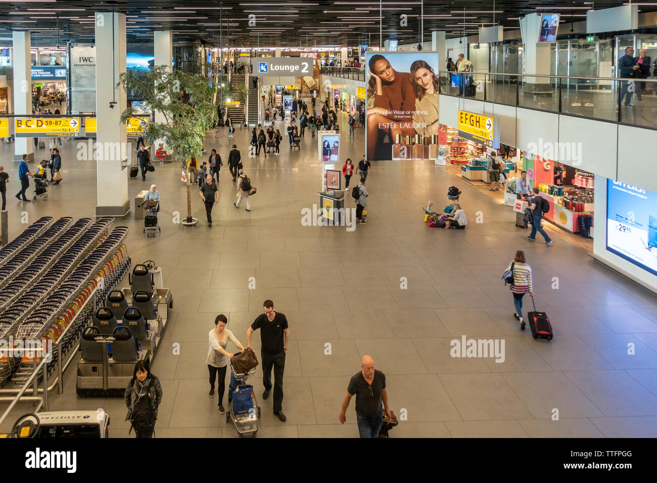 Ansicht der Bahnhofshalle o fDeparture Lounge 2 am Flughafen Schiphol, Amsterdam, mit Reisenden, Shops, Werbung, Trolleys, Hilfe Buggys. Stockfoto