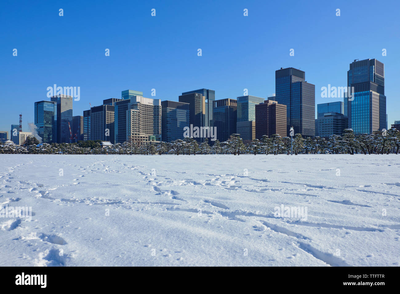 Verschneite Feld durch moderne Gebäude gegen blauen Himmel während der sonnigen Tag Stockfoto