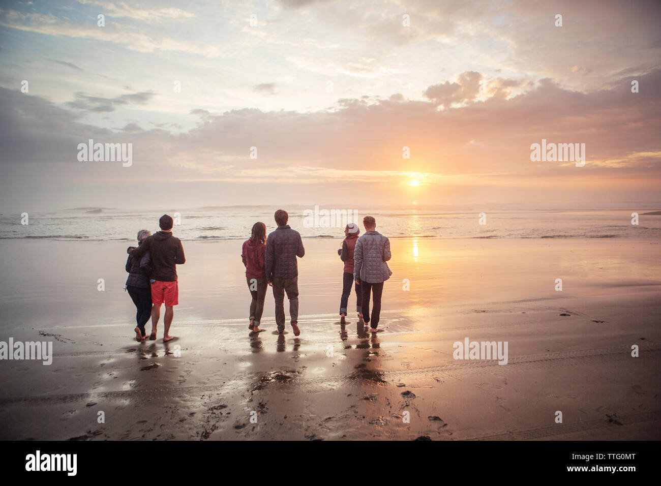 Rückansicht der Paare zu Fuß am Ufer am Strand bei Sonnenuntergang Stockfoto