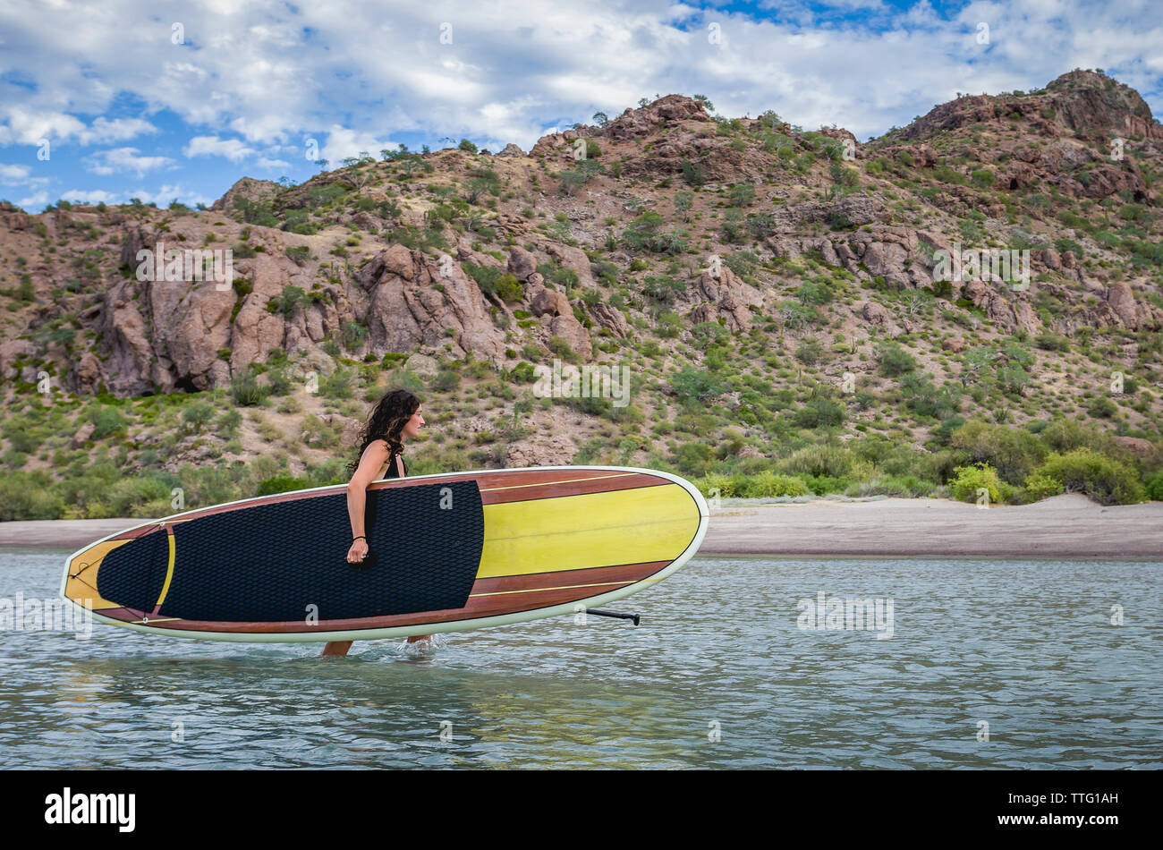 Frau, die trägt Paddleboard im Meer gegen Berg Stockfoto