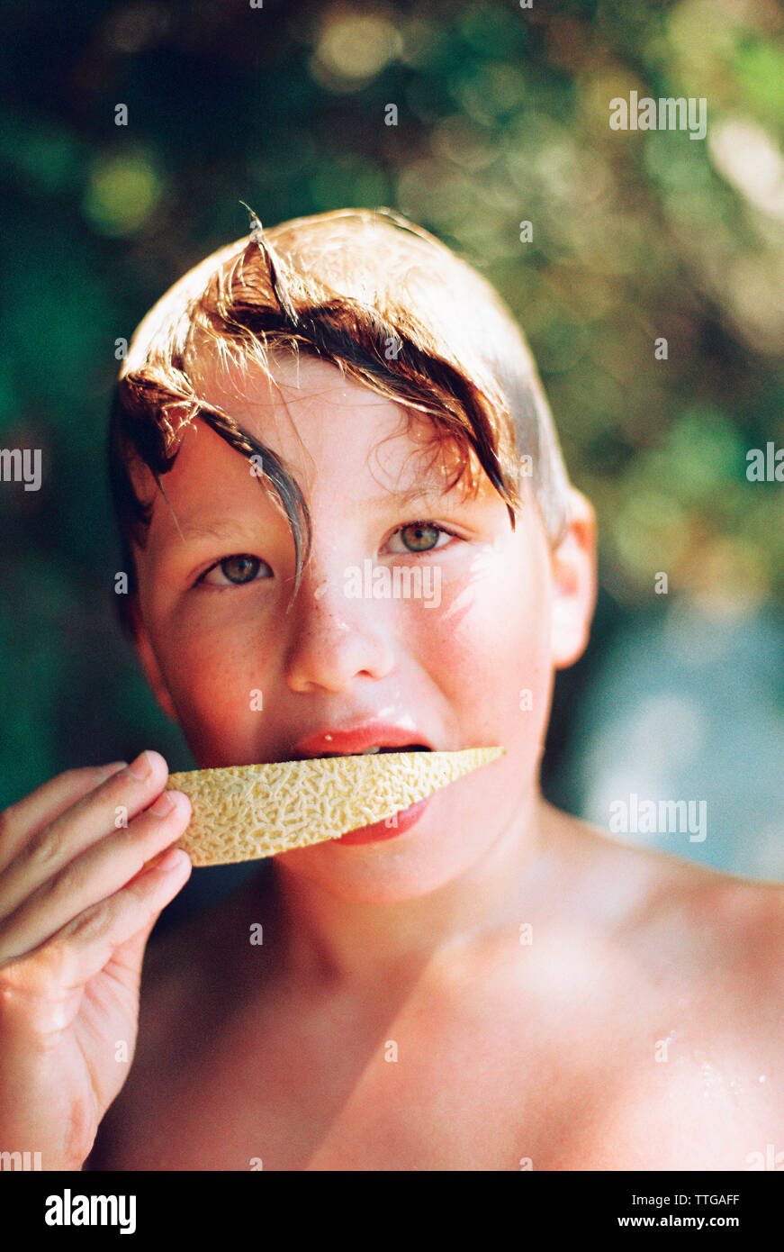 Junge schaut in die Kamera während des Essens eine Melone Stockfoto