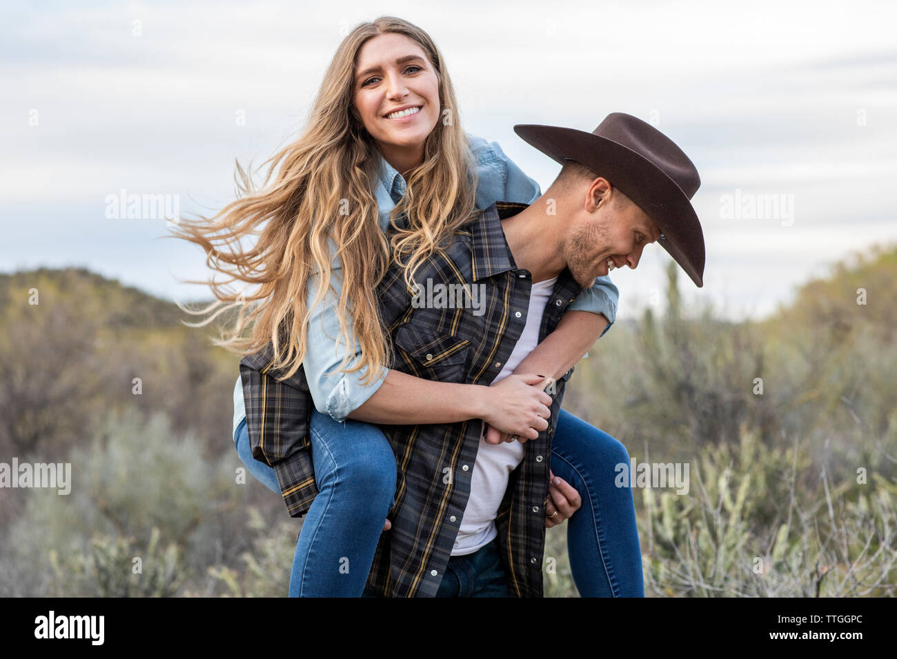 Western Wear junges Paar, Huckepack Fahrt auf der Ranch Stockfoto