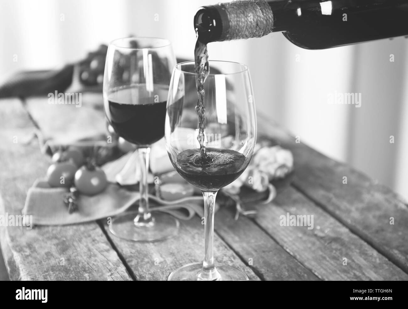 Gießen Wein in Glas auf Holztisch, getönt in Schwarz und Weiß Stockfoto