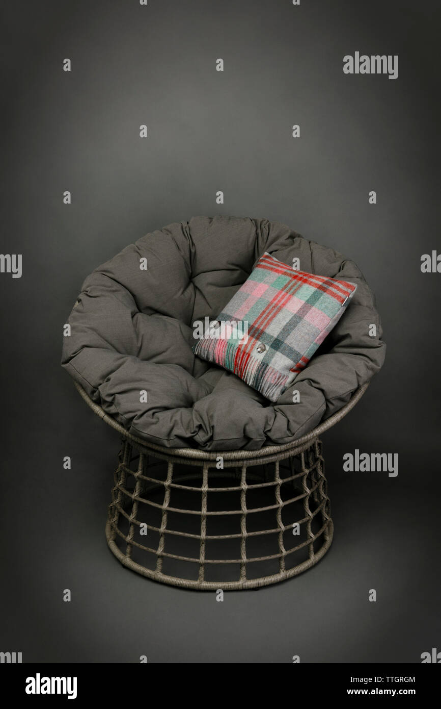Korbstuhl und weichen Sitzkissen und einem bunten Kissen auf grauem Hintergrund Stockfoto