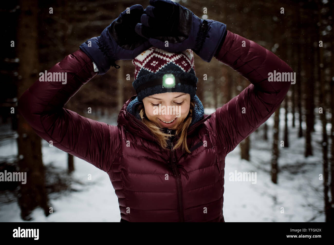 Lächelnde Frau glücklich mit Stirnlampe auf draußen in den verschneiten Wald Stockfoto
