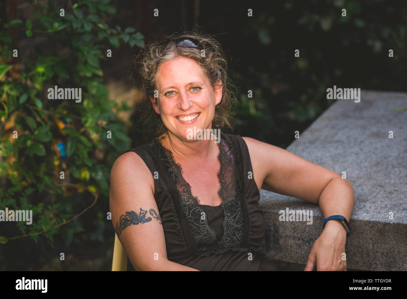 Portrait von lächelnden Frau sitzt gegen Pflanzen im Garten Stockfoto