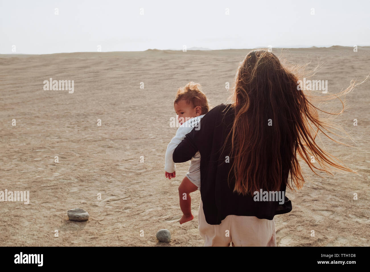 Zurück Blick auf eine Frau, die zu Fuß in der Wüste während Ihr Baby Holding Stockfoto