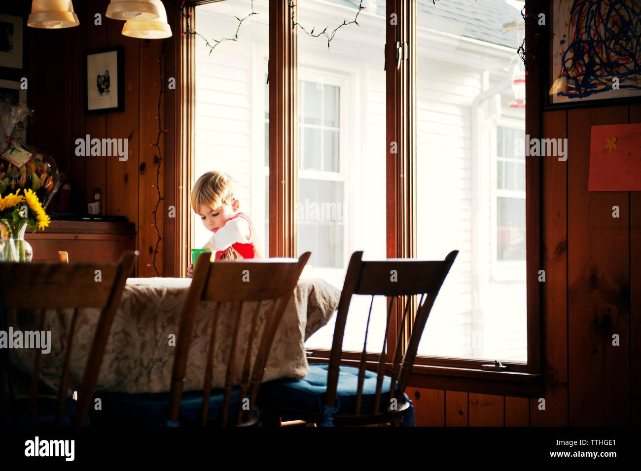 Junge an Esstisch gegen Fenster zu Hause Stockfoto