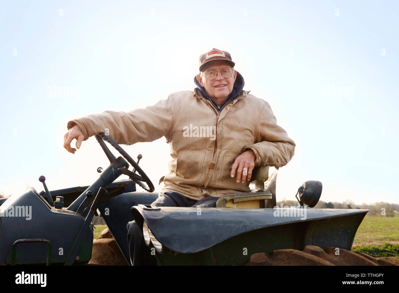 Portrait von zuversichtlich Landwirt Fahren des Traktors gegen Sky Stockfoto