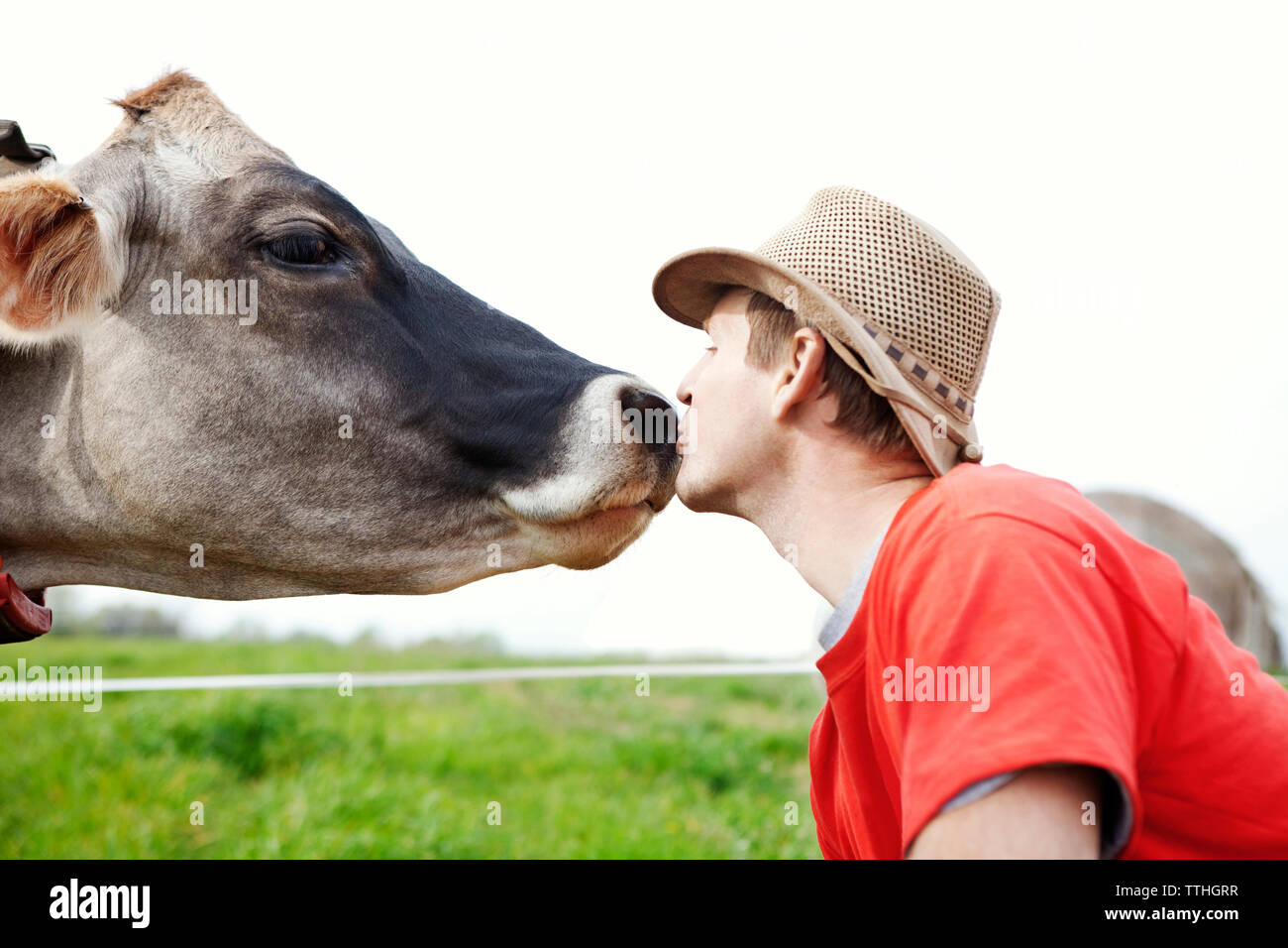 Seitenansicht des Menschen küssen Kuh auf der Wiese gegen Sky Stockfoto