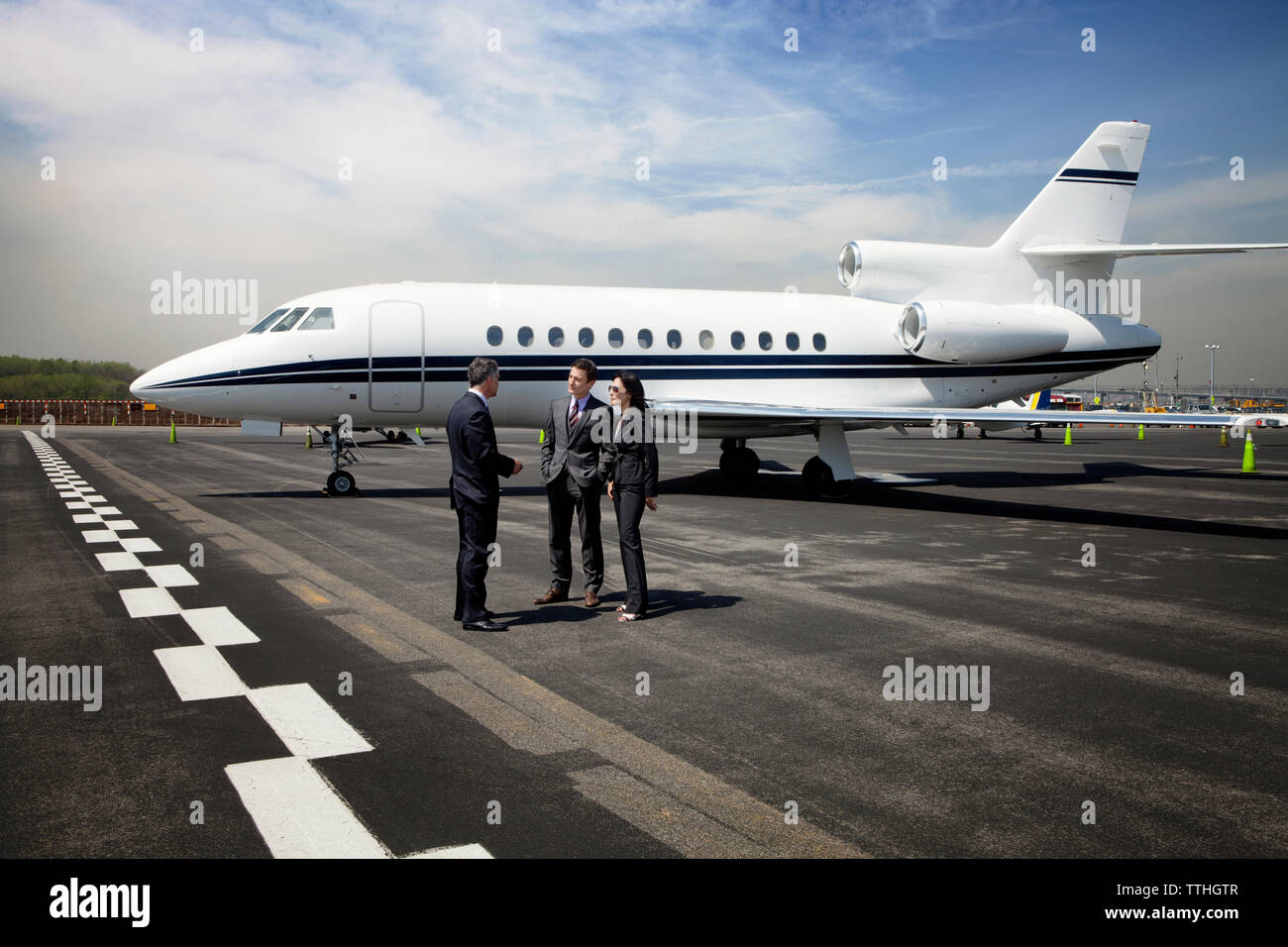 Geschäftsleute diskutieren, während sie gegen den Unternehmensjet auf der Landebahn stehen Stockfoto