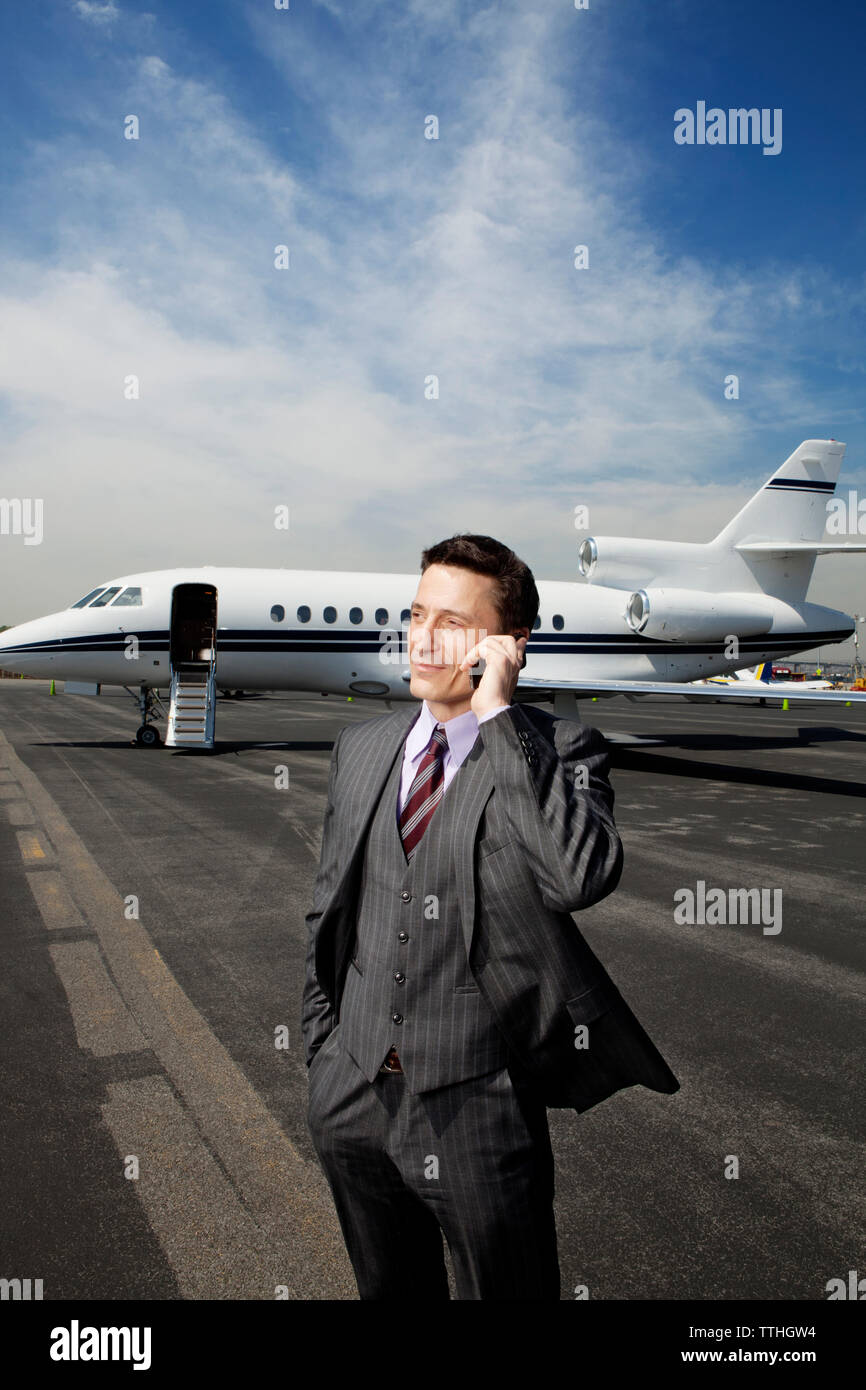 Geschäftsmann, der telefoniert, während er auf der Landebahn gegen den Unternehmensjet steht Stockfoto