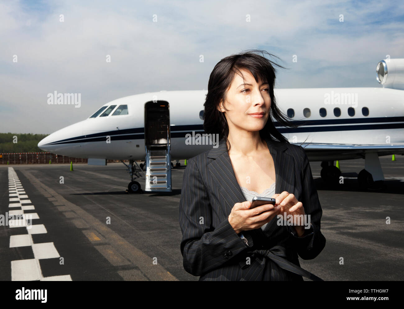 Nachdenklich Geschäftsfrau, Telefon, während sich gegen Corporate Jet auf Start- und Landebahn Stockfoto
