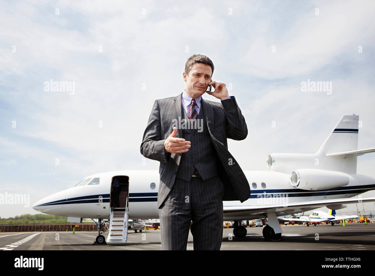 Geschäftsmann, der am Telefon kommuniziert, während er auf der Landebahn gegen den Unternehmensjet steht Stockfoto