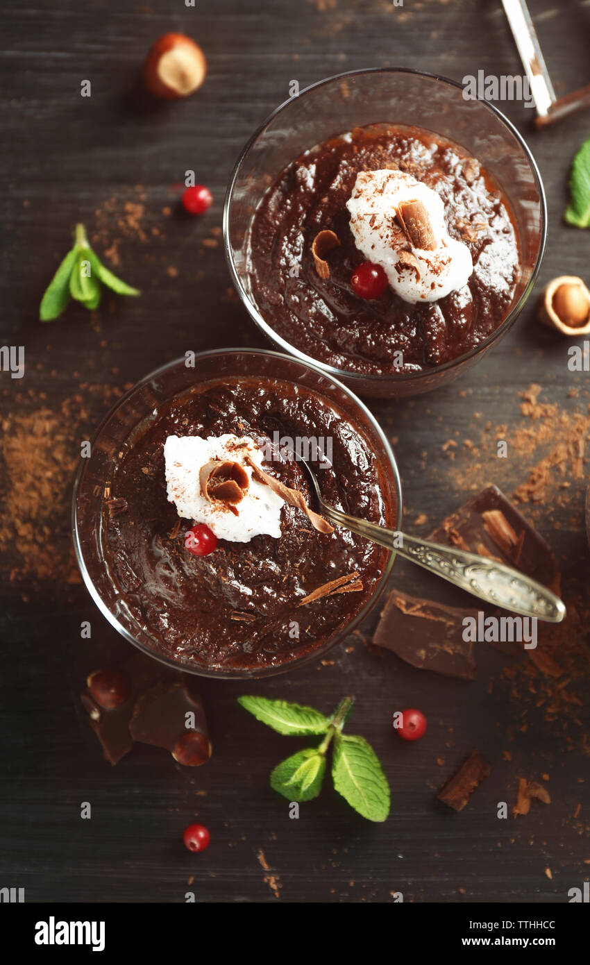 Glas Tassen Schokolade Dessert mit Preiselbeeren, frischer Minze und aufgeschäumter Milch auf schwarzen Holztisch Stockfoto