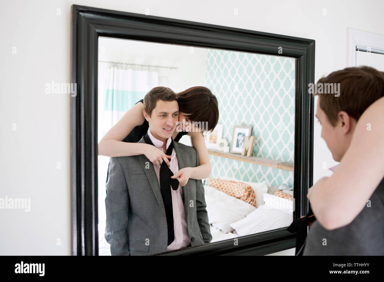 Lächelnde Frau binden Freund krawatte vor Spiegel Stockfoto