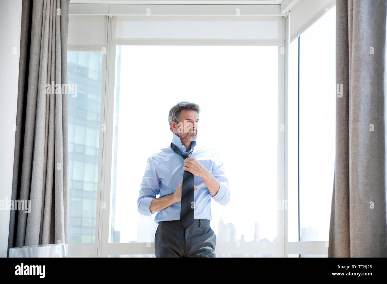 Geschäftsmann binden Krawatte beim Ständigen gegen Fenster im Hotel Zimmer Stockfoto