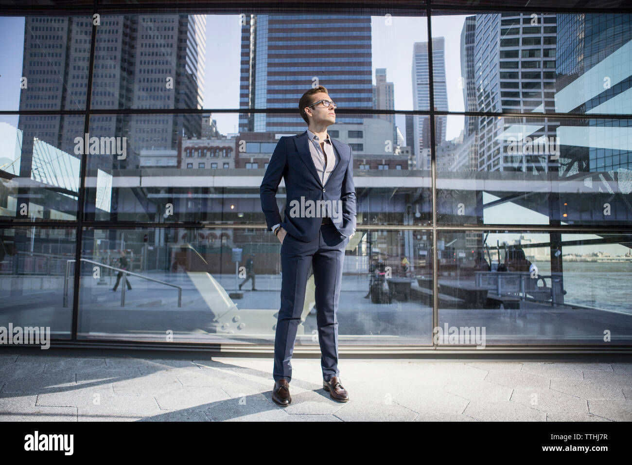 Geschäftsmann mit Händen in den Taschen, der hochblickt, während er gegen ein modernes Gebäude steht Stockfoto