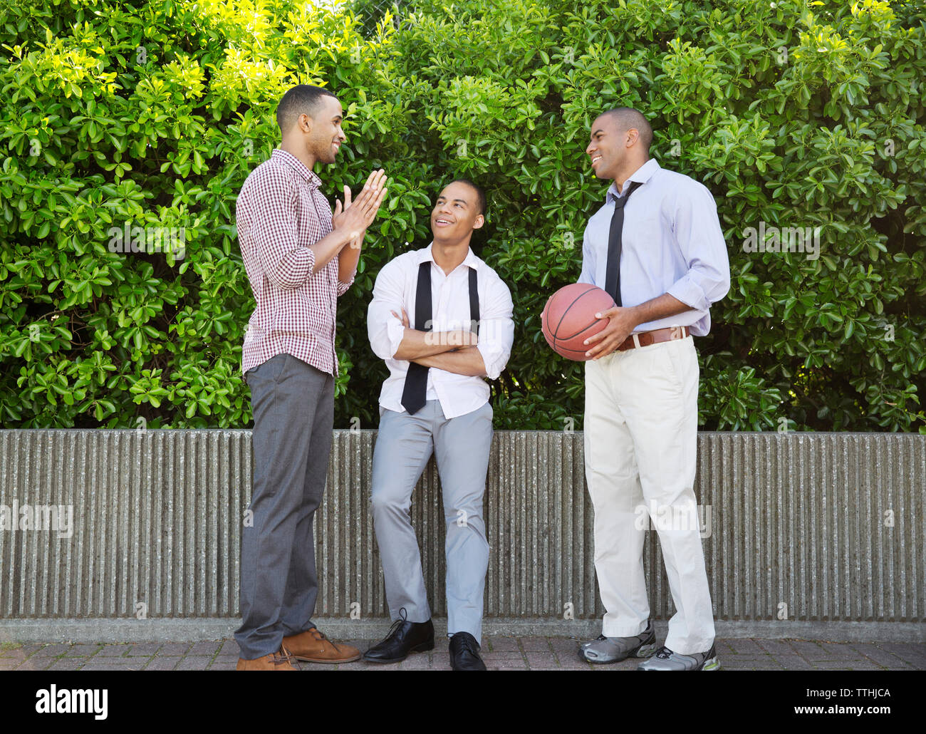 Lächelnder Mann mit Basketball, während im Gespräch mit Freunden gegen Pflanzen Stockfoto