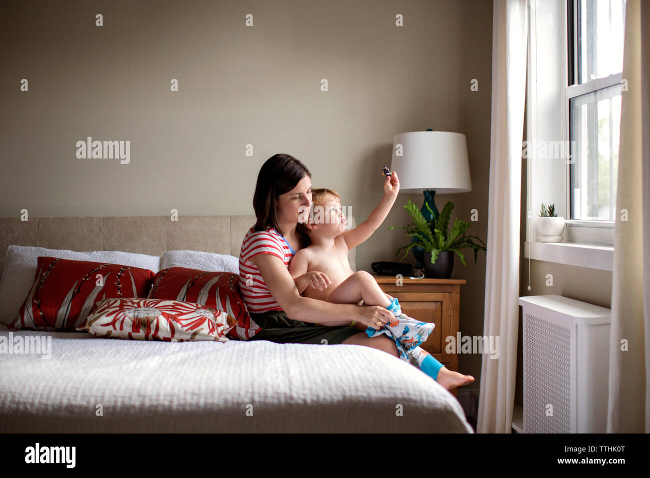 Mutter dressing verspielten Sohn beim Sitzen auf dem Bett Stockfoto