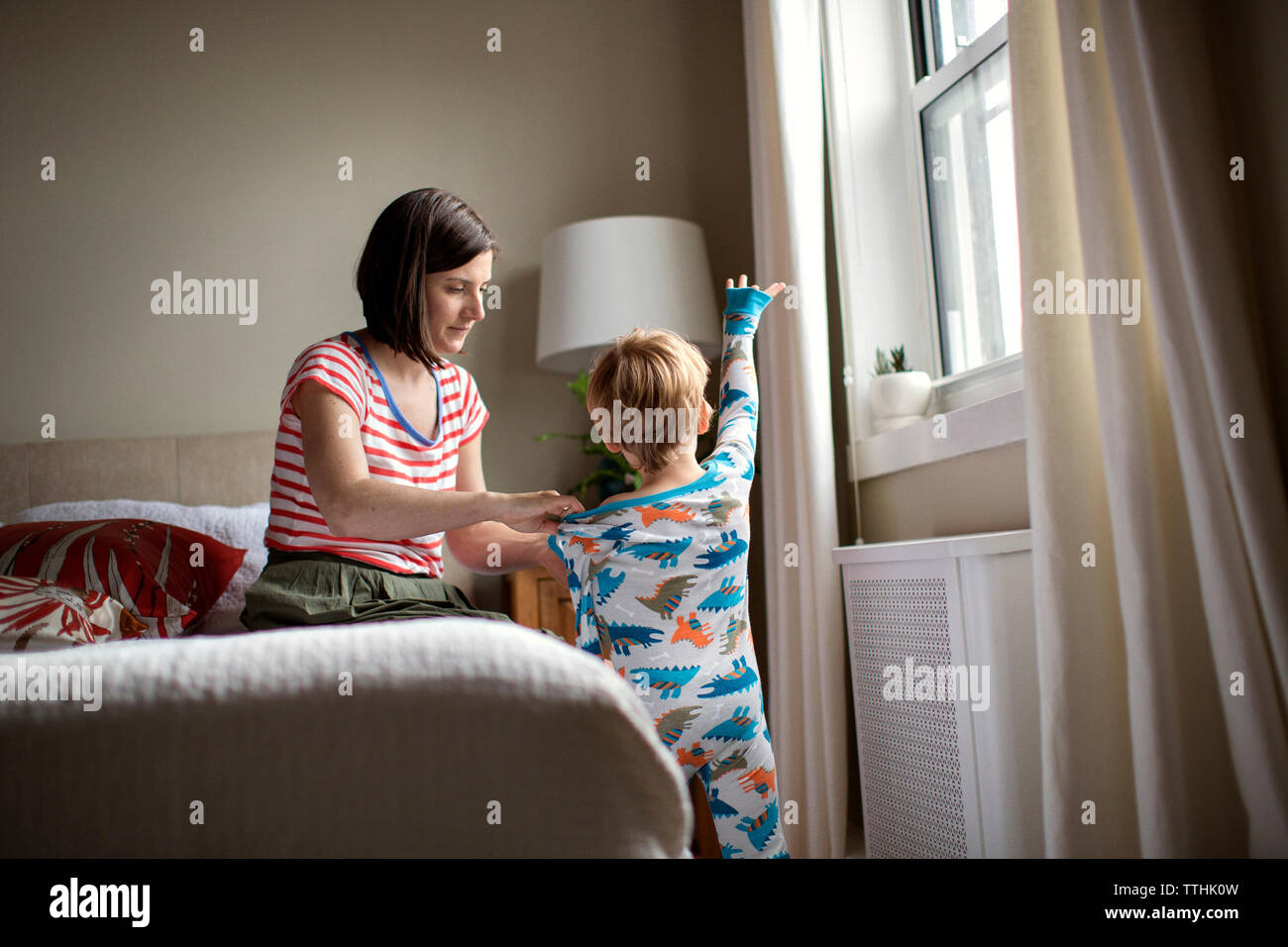 Mutter dressing Sohn beim Sitzen auf dem Bett im Zimmer Stockfoto