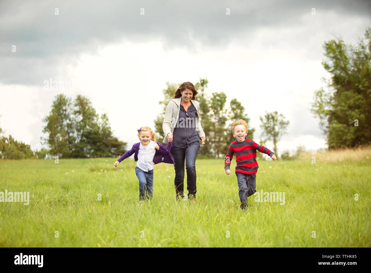 Glückliche Mutter Wandern mit Kindern auf der Wiese gegen Sky Stockfoto