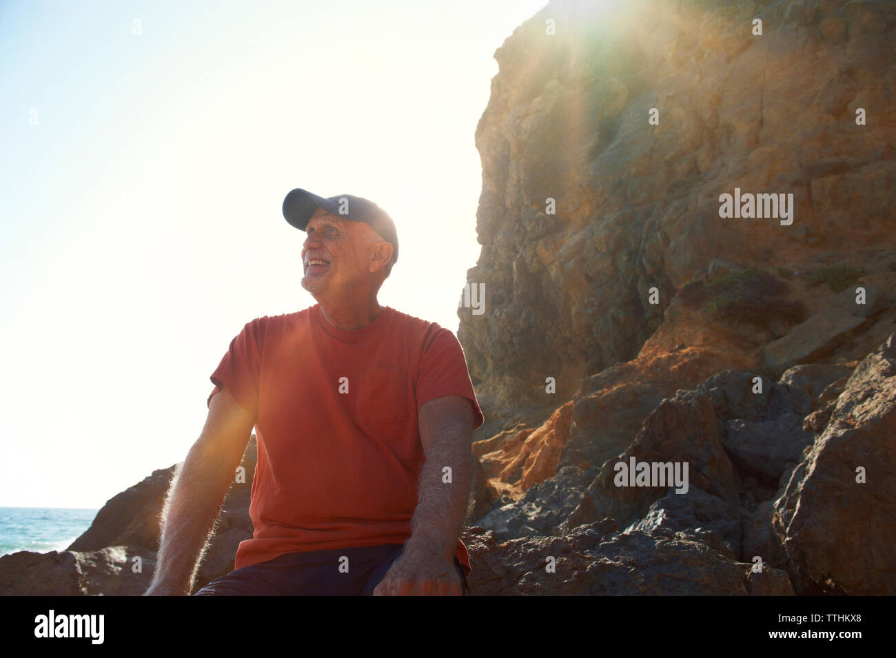 Gerne älterer Mann sitzt auf Felsen während der sonnigen Tag Stockfoto