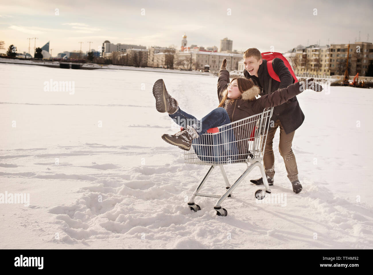 Glückliche Menschen drücken Freundin in Warenkorb sitzen auf schneebedeckten Feld Stockfoto