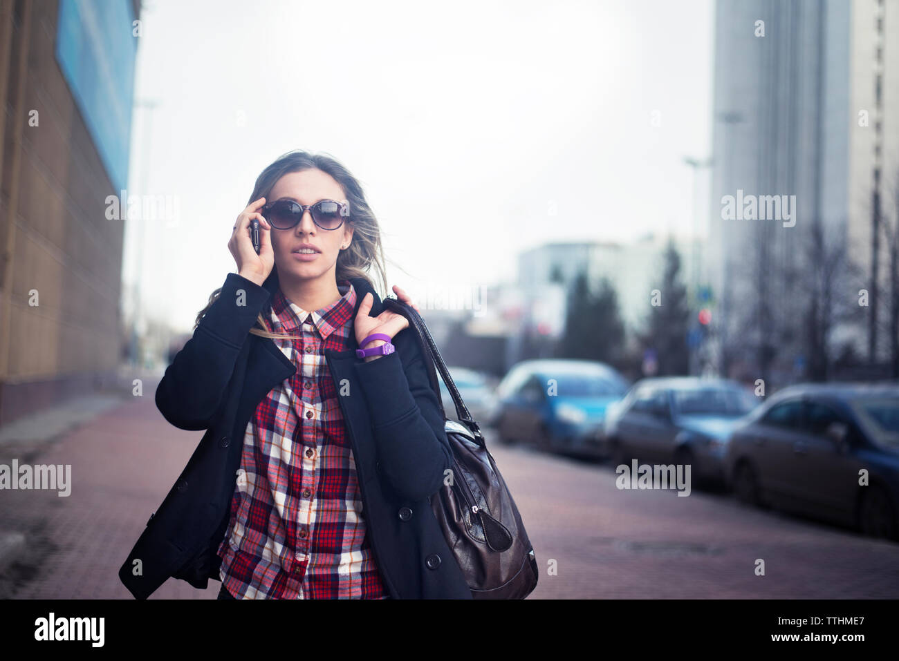 Junge Frau mit Sonnenbrille, die Schultertasche in Stadt Stockfoto