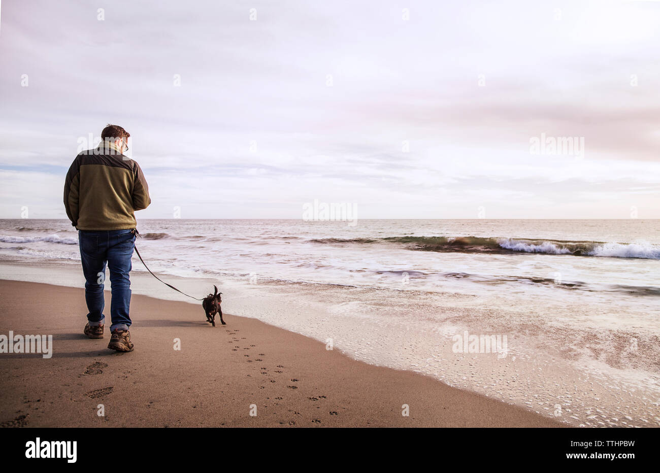 Ansicht der Rückseite des Mann mit Hund Wandern am Ufer gegen bewölkter Himmel Stockfoto