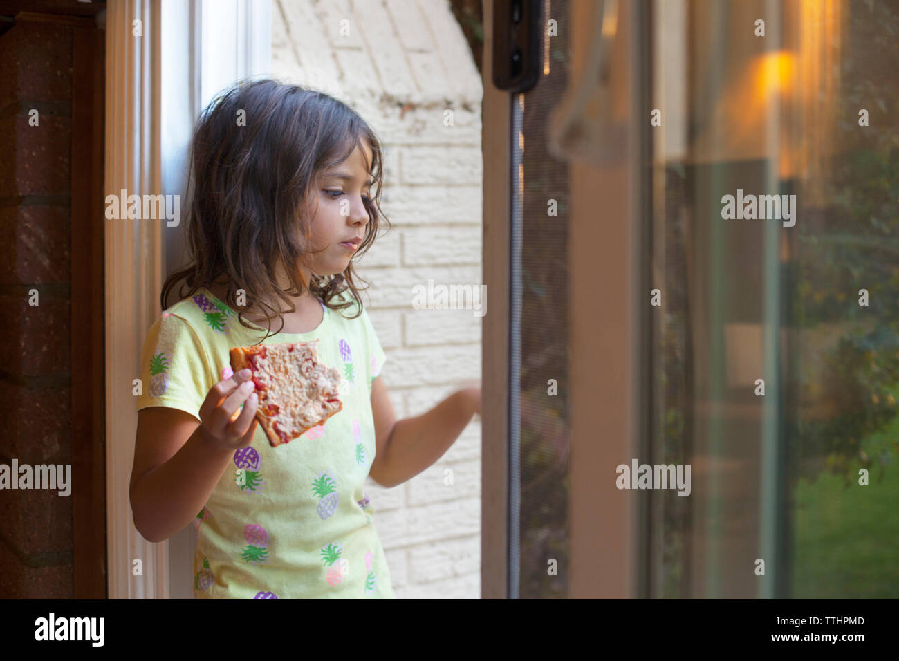 Nachdenkliches Mädchen, dass Pizza, während Sie aus dem Fenster zu hause suchen Stockfoto