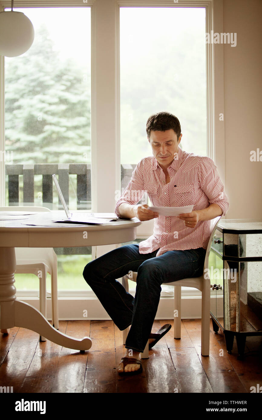 Mann lesen Dokument beim Sitzen auf Stuhl von Tisch zu Hause Stockfoto