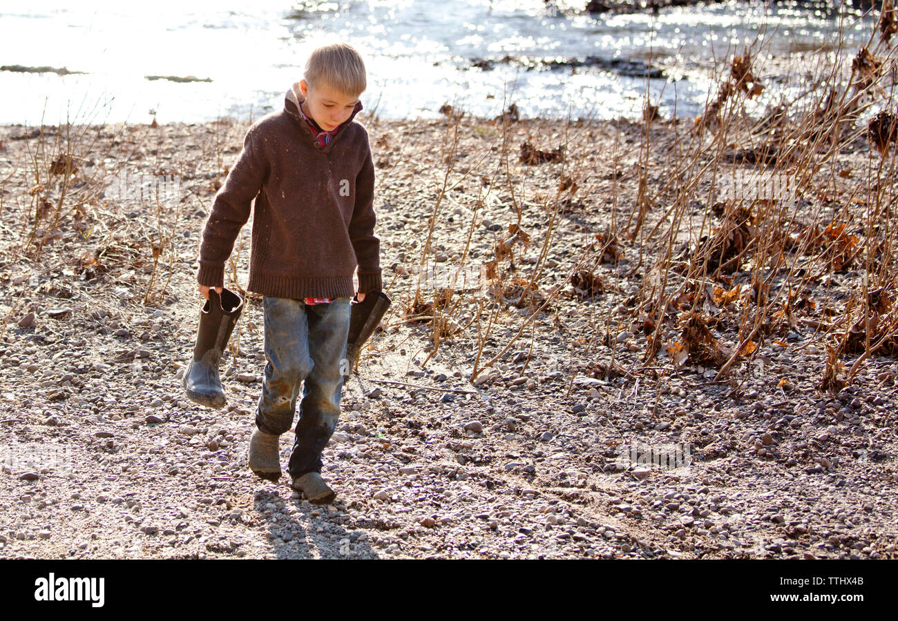 Junge die Gummimanschette beim Gehen auf Feld, Fluss Stockfoto