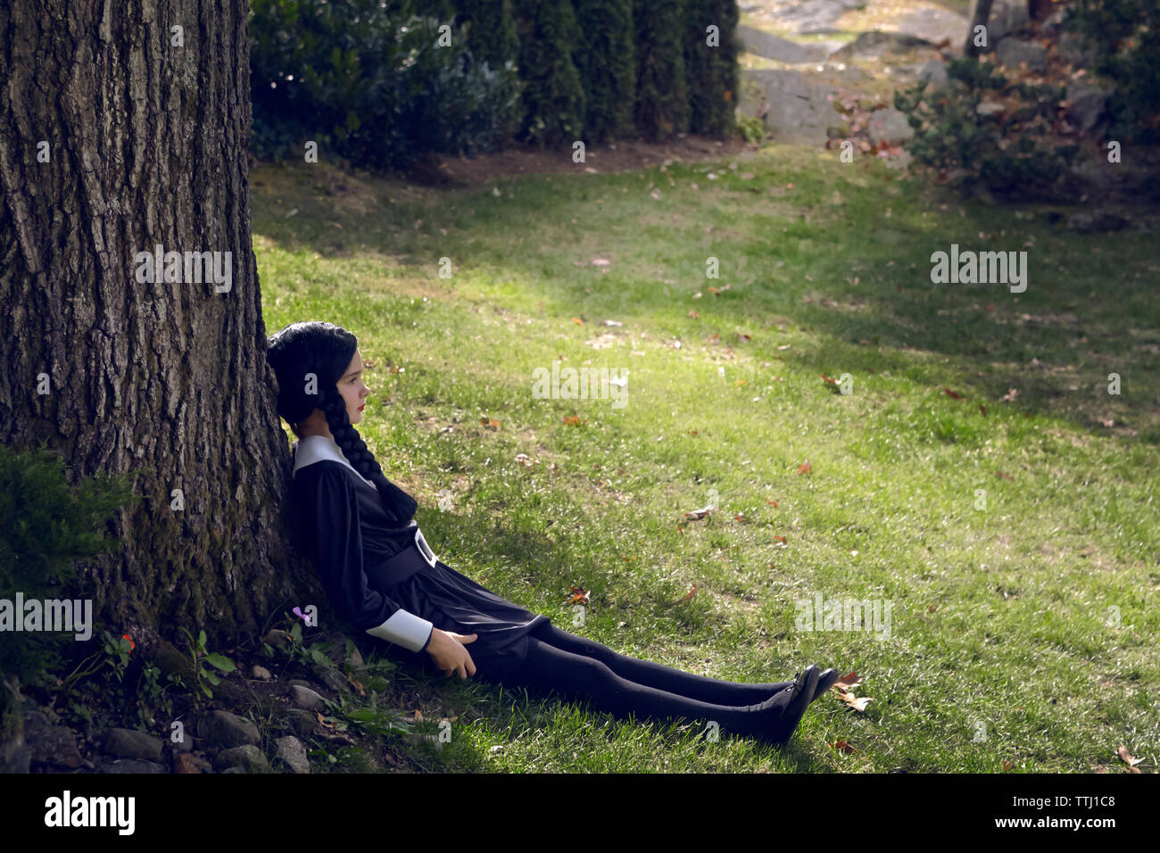 Mädchen von Baumstamm sitzen auf Feld in Rasen Stockfoto