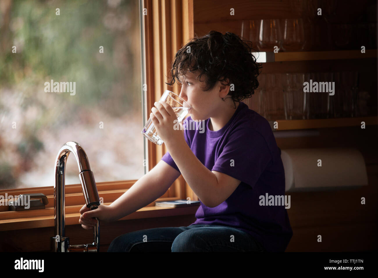 Junge Trinkwasser beim Sitzen am Küchentisch in Home Stockfoto
