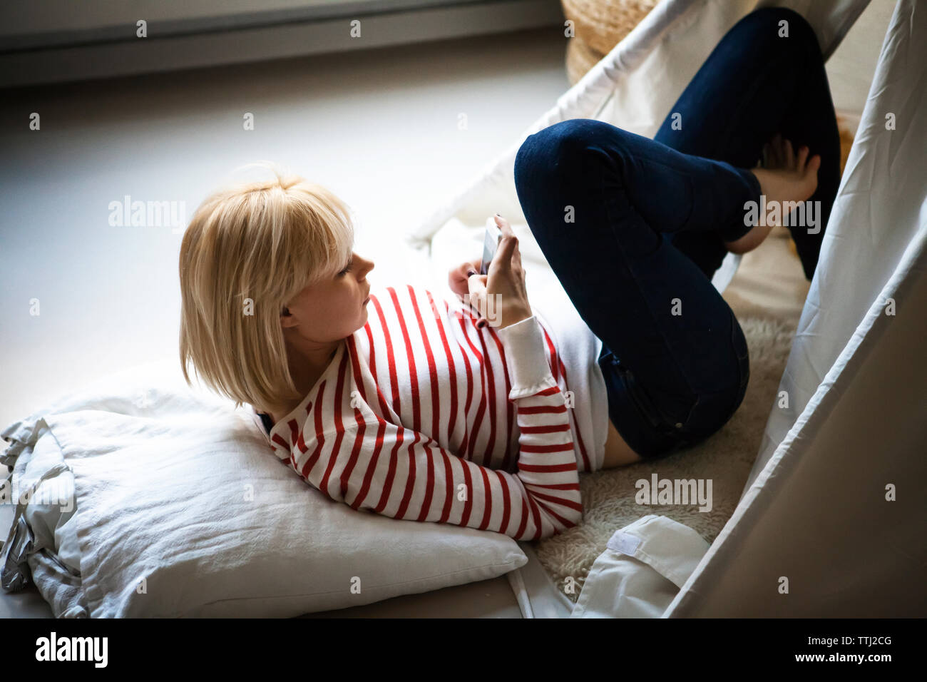Frau mit Smart Phone beim Liegen im Zelt zu Hause Stockfoto