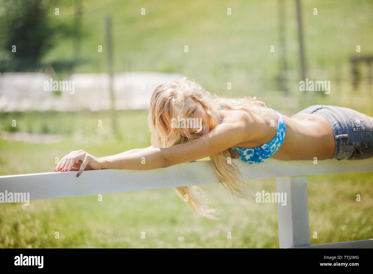 Lächelnde Frau liegend auf Zaun auf dem Feld Stockfoto