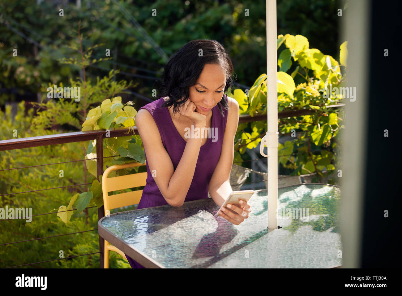 Frau mit Smart Phone beim Sitzen auf Stuhl, Tisch, Balkon Stockfoto