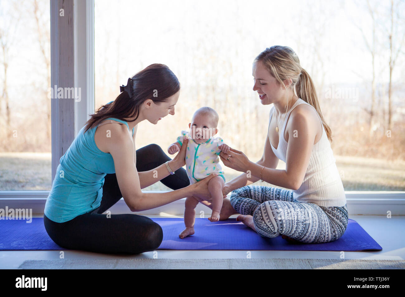 Fröhliche homosexuelle Frauen spielen mit Baby Girl auf der Trainingsmatte zu Hause Stockfoto