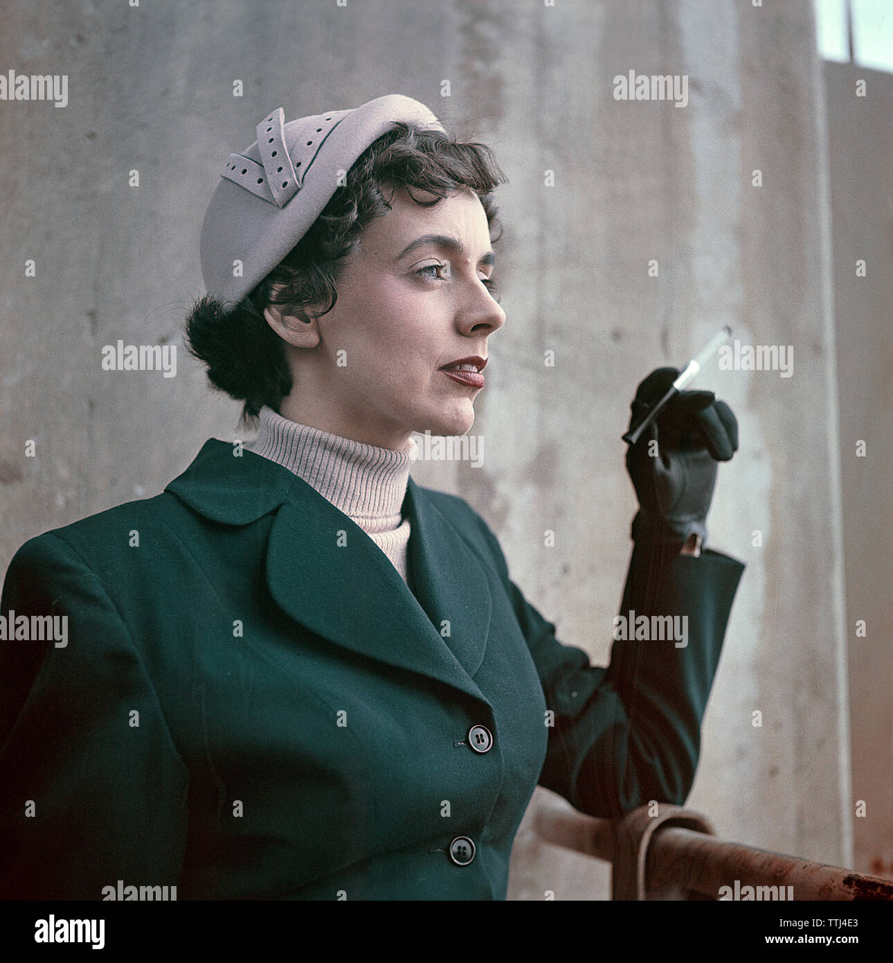 1950er Jahre Damenmode. Eine schwedische junge Frau trägt einen typischen 50er Outfit. Eine grüne Jacke und einem passenden hut. Sie verwendet eine zigarettenspitze. Schweden 1950. CV 5-11 Stockfoto