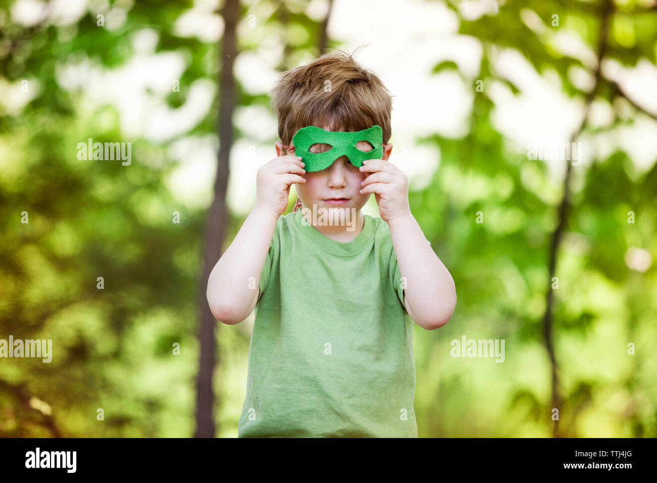 Junger Mann, Augenmaske, während sich gegen Bäume am Spielplatz Stockfoto