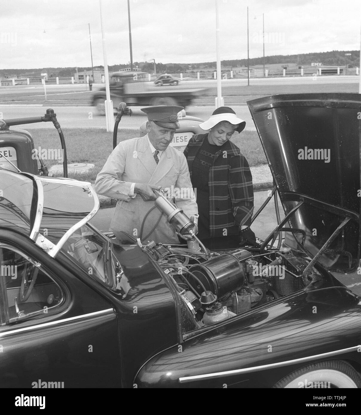 Auto Besitzer der 1950er Jahre. Eine Frau hat an einer Tankstelle angehalten und ist die Hilfe eines Mannes mehr Motoröl füllen. Schweden 1954. Kristoffersson ref BP 35-11 Stockfoto